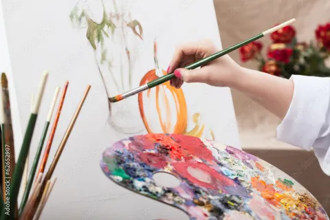 Hand holding paintbrush, touching canvas with paint.
