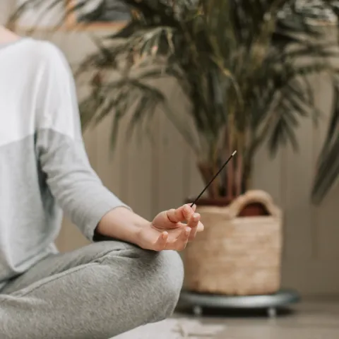 view of half a person sitting on floor with legs crossed and hand resting, with fingers pinched