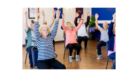 Senior adults sitting in chairs with arms raised doing exercises